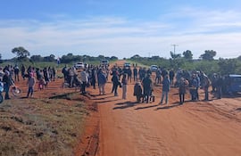 Un grupo de personas discute en un camino rural con chaquetas y gorros, mientras una bandera paraguaya ondea al fondo.