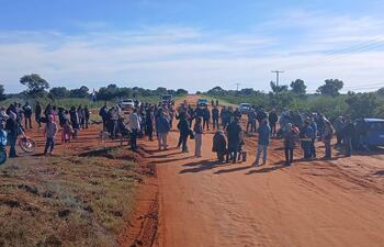 Un grupo de personas discute en un camino rural con chaquetas y gorros, mientras una bandera paraguaya ondea al fondo.