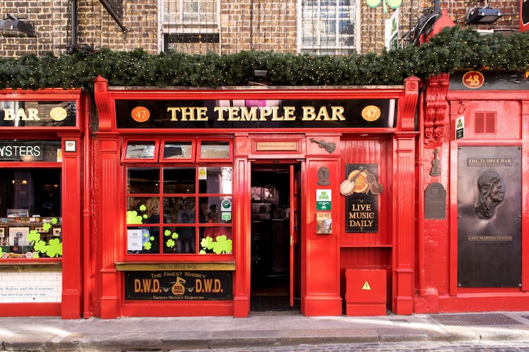 Fachada del bar Temple Bar, color rojo vibrante con letreros dorados, no hay personas visibles en el entorno urbano.