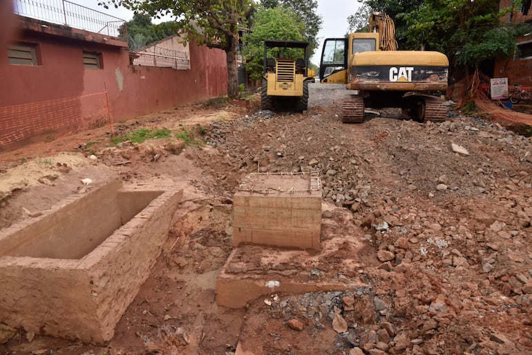Maquinaria de construcción en obra, incluyendo una retroexcavadora CAT y un tractor amarillo, en un entorno urbano con edificios y árboles.