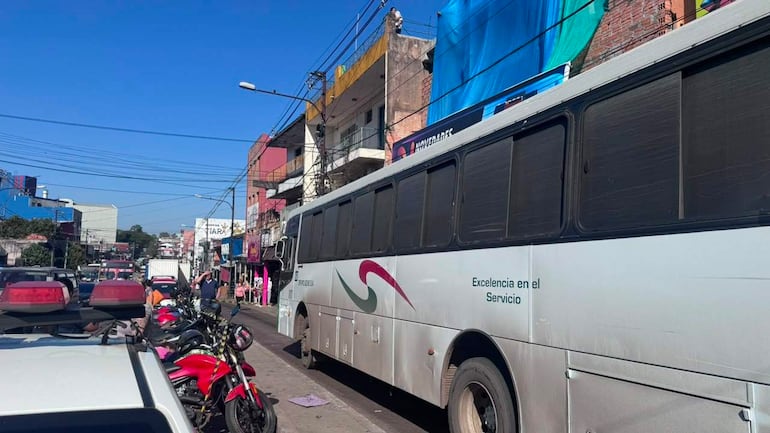 Escena urbana con autobús de transporte urbano estacionado, varias motos aparcadas y edificios coloridos de fondo.