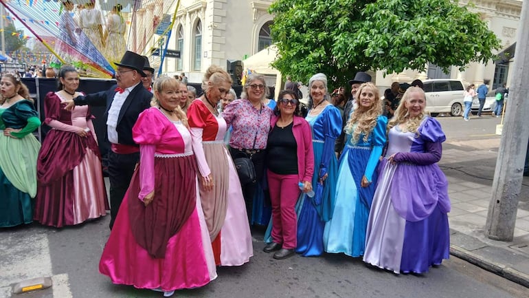Mujeres con vestidos coloridos sonríen en un ambiente festivo, mientras un hombre con sombrero se encuentra en el centro del grupo.