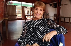 Mirtha Ibarra con blusa negra y lunares blancos, sonríe mientras se sienta en un ambiente acogedor con mesas y sillas.