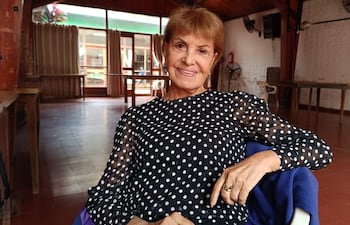 Mirtha Ibarra con blusa negra y lunares blancos, sonríe mientras se sienta en un ambiente acogedor con mesas y sillas.