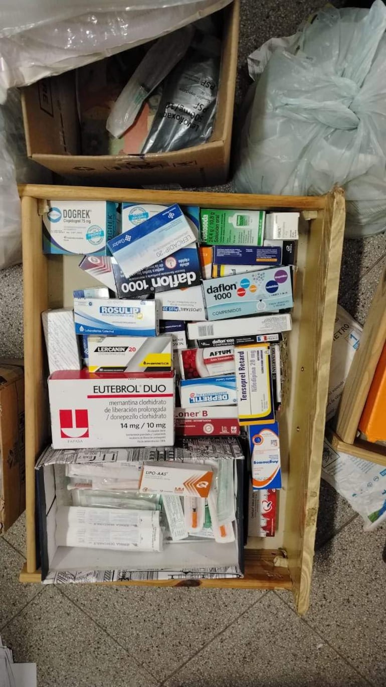 Cajón de madera repleto de cajas de medicamentos variados en un entorno desorganizado y oscuro.