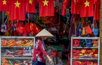 Una mujer pasa junto a una tienda que vende camisetas y banderas con la bandera nacional vietnamita en in Hanoi , Vietnam (Photo by Nhac NGUYEN / AFP)