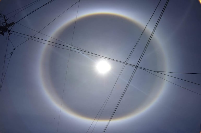 Fenómeno natural de halo solar con cielo gris azulado y líneas de cables eléctricos cruzando la imagen.
