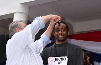 Alfredo Bonga, con etiqueta 'BICHO N° 34', sonríe mientras un profesional le atiende en un evento con decoraciones en los colores paraguayos.