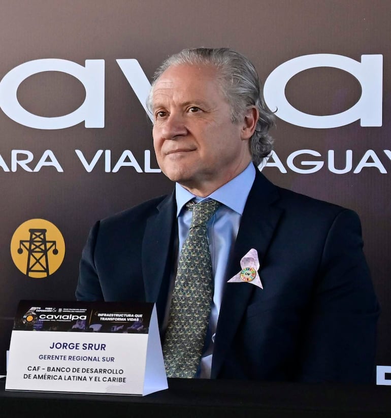 Jorge Srur sentado en una mesa, con cabello canoso y corbata decorada, frente a un fondo institucional del CAF.
