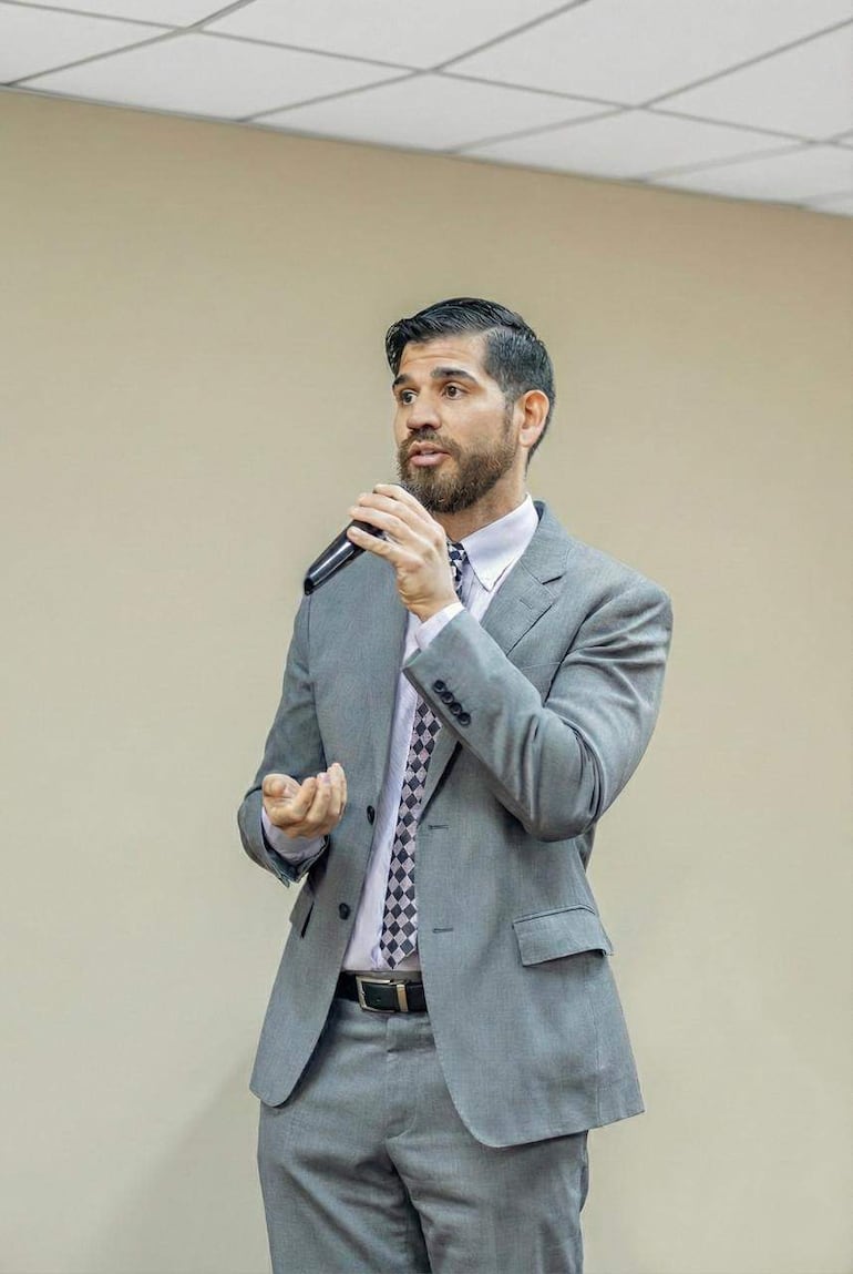 Eduardo Velázquez Romero, vestido con traje gris y corbata, habla serio al micrófono en un entorno interior con pared beige.