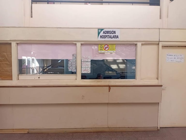 Área de admisión vacía con cartel que dice 'ADMISIÓN HOSPITALARIA', paredes claras y ventanilla administrativa reflejando un ambiente organizado.