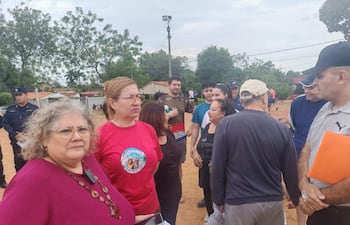 Dos mujeres en el centro conversan; una lleva blusa fucsia y la otra camiseta colorida, con un oficial de policía presente.