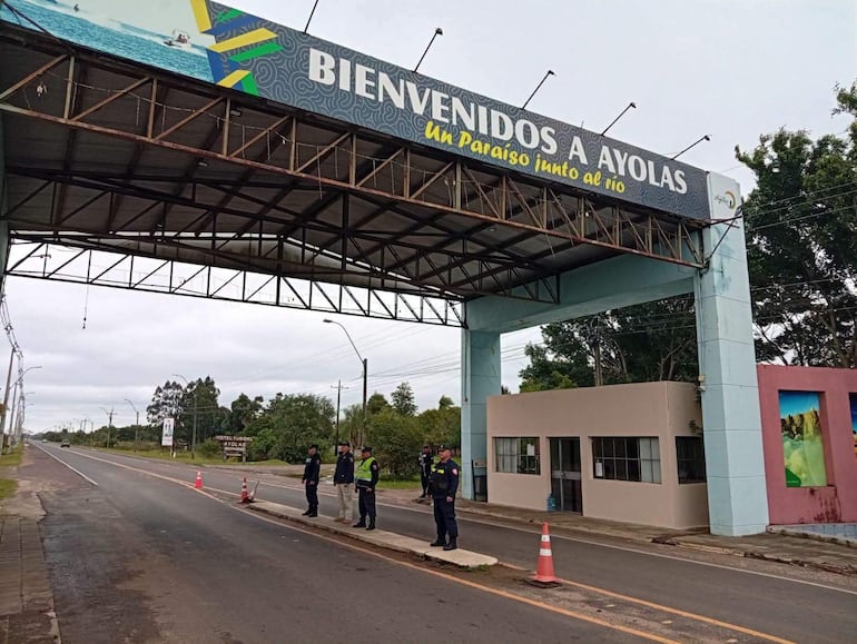 Seis policías uniformados en control junto a arco de bienvenida a Ayolas con vegetación al fondo.