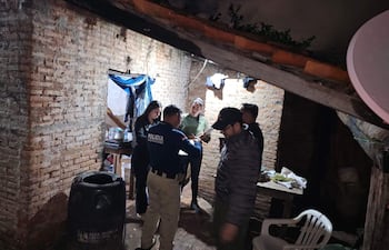 Un policía con uniforme interactúa con una mujer de suéter negro, mientras otros observan la escena en un ambiente sombrío.