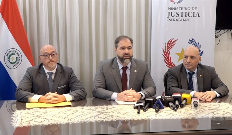Rodrigo Nicora con traje oscuro, Rubén Maciel con barba hablando y Óscar Pereira atento en conferencia de prensa con micrófonos y bandera detrás.