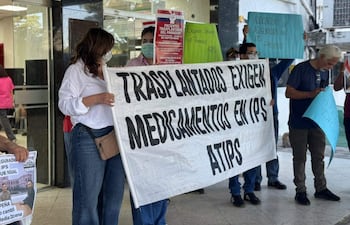 Mujer sostiene pancarta blanca sobre medicación, rodeada de manifestantes con carteles en el Hospital Central del IPS.