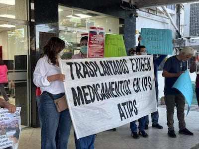 Mujer sostiene pancarta blanca sobre medicación, rodeada de manifestantes con carteles en el Hospital Central del IPS.