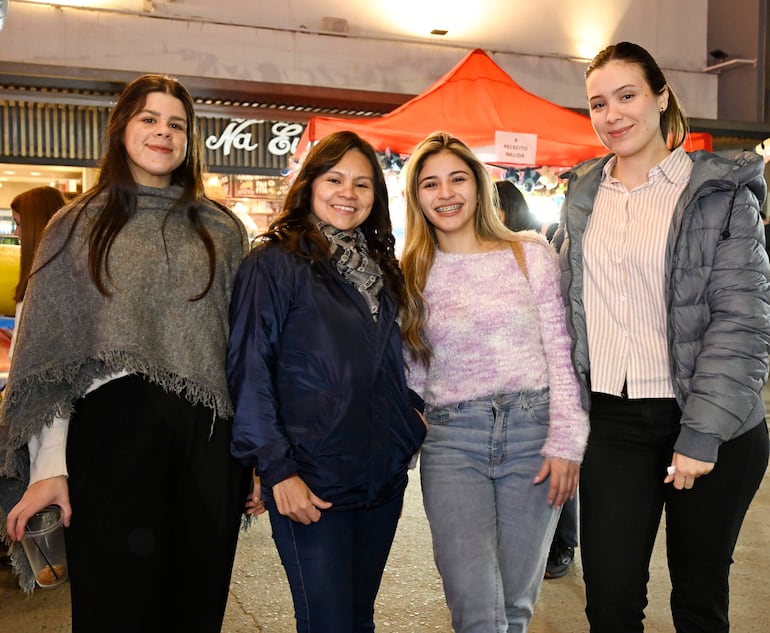 Cuatro mujeres sonrientes, una con poncho gris, otra en chaqueta oscura, una más en suéter claro y otra en chaqueta gris claro, posan alegremente.