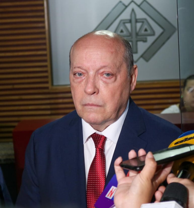 César Diesel en traje oscuro con expresión seria, rodeado de periodistas que sostienen micrófonos y cámaras.