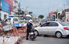 La imagen muestra una calle con varios vehículos estacionados y en movimiento, pero no hay personas visibles en la escena. En el primer plano, se observa un bache grande y profundo en la acera, lleno de escombros y trozos de madera, además de algunos cables expuestos que parecen ser parte de la infraestructura urbana.
El ambiente es urbano y exterior, característico de una vía de tránsito; hay una fila de vehículos en sentido contrario y algunos en la dirección opuesta. No se identifican elementos visuales que correspondan a un equipo de fútbol, ni lugares reconocibles como estadios o monumentos. La situación podría interpretarse como un posible peligro para los transeúntes y conductores, dadas las condiciones del bache y los escombros a la vista.