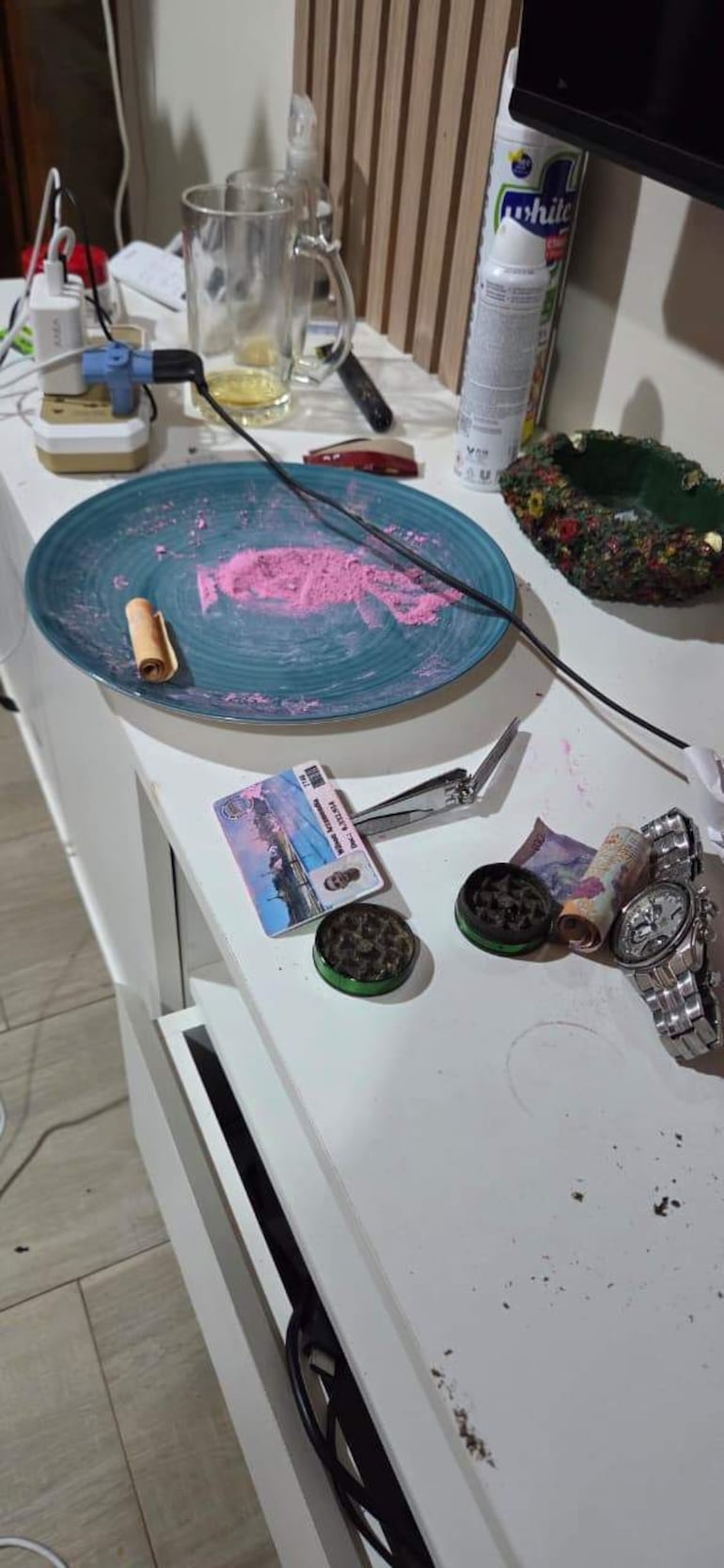 Mesa desordenada con polvo rosa, billetes y grinders, sin personas visibles en la escena.