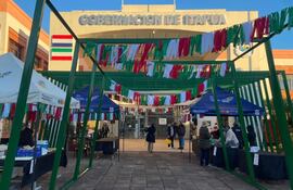 Carpas de colores en la Gobernación de Itapúa, con personas interactuando y ofreciendo comidas típicas en un ambiente festivo.