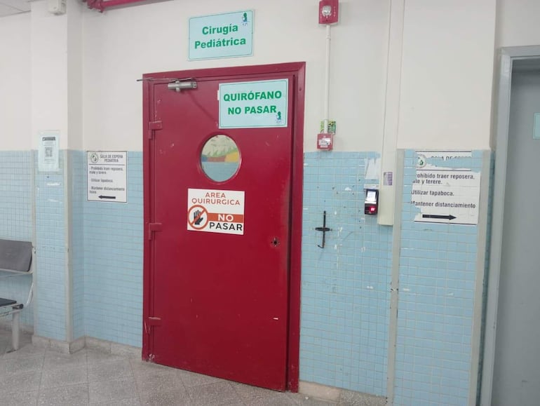 Puerta roja de quirófano en ambiente hospitalario, con letrero que indica normas de acceso y uso de tapaboca.