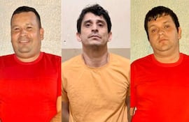 Cuatro hombres detenidos, dos en camiseta roja, uno en amarilla y otro en gris oscuro, con expresiones serias frente a una pared simple.