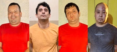 Cuatro hombres detenidos, dos en camiseta roja, uno en amarilla y otro en gris oscuro, con expresiones serias frente a una pared simple.