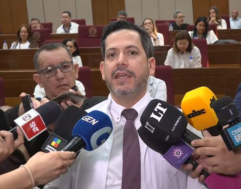 Raúl Latorre en corbata y camisa blanca, hablando a la prensa rodeado de micrófonos en un entorno institucional.