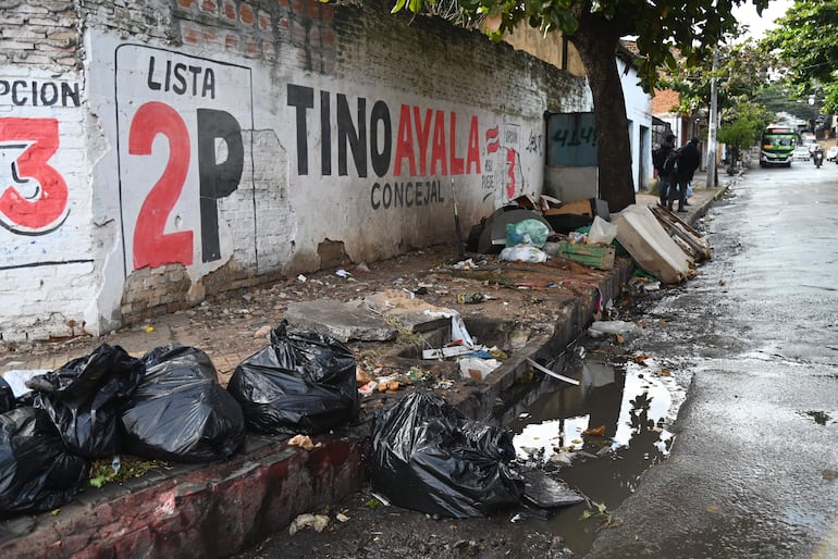 Mural en pared de ladrillo con inscripción 'Tino Ayala Concejal', entorno urbano descuidado y pavimento húmedo.