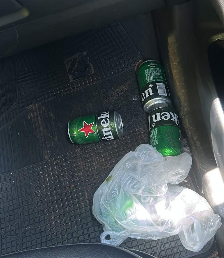 Interior de auto con latas de cerveza Heineken y Kenty en el suelo, y una bolsa de plástico con más latas a la derecha.