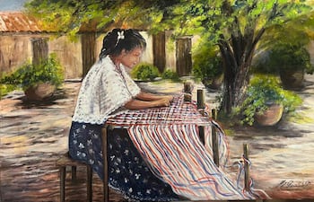 Mujer con vestido oscuro y manta blanca teje en un telar, rodeada de árboles y casa de adobe.