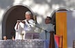 Sacerdotes con vestimentas litúrgicas blancas en ceremonia religiosa al aire libre, sosteniendo patena y cáliz, mientras la comunidad escucha.