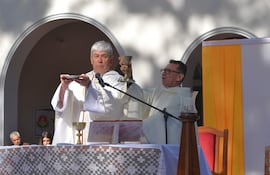 Sacerdotes con vestimentas litúrgicas blancas en ceremonia religiosa al aire libre, sosteniendo patena y cáliz, mientras la comunidad escucha.