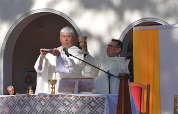 Sacerdotes con vestimentas litúrgicas blancas en ceremonia religiosa al aire libre, sosteniendo patena y cáliz, mientras la comunidad escucha.