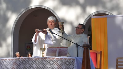 Sacerdotes con vestimentas litúrgicas blancas en ceremonia religiosa al aire libre, sosteniendo patena y cáliz, mientras la comunidad escucha.