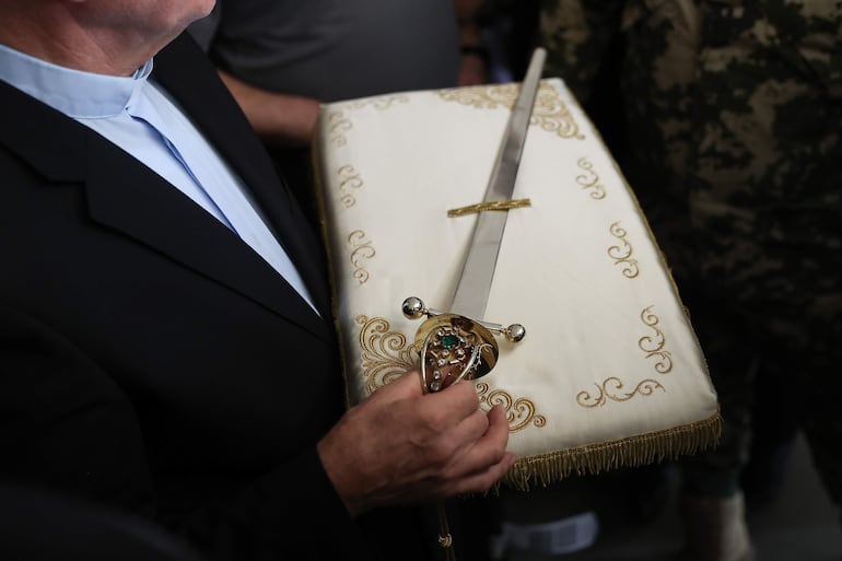 El Rector de la Basílica Santuario de San Miguel Arcángel, Ladislao Suchy, sostiene la espada de San Miguel Arcángel este jueves en el Aeropuerto Internacional Silvio Pettirossi.