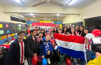 Niños y adolescentes sonrientes del CEPB, visten camisetas rayadas rojas y blancas, sosteniendo globos y una bandera del Club Olimpia.