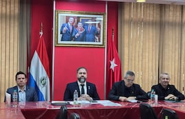 Rodrigo Nicora y otros diputados en traje negro sentados en mesa con banderas de Paraguay y Turquía, revisando documentos.