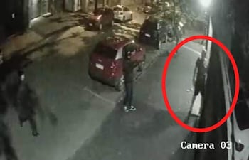 Tres personas en una calle oscura, dos de pie conversando y una más alejada en medio de un ambiente nocturno.