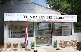 Tienda Penitenciaria exhibiendo estantes con productos, logotipo del Ministerio de Justicia y la bandera paraguaya en un entorno soleado.