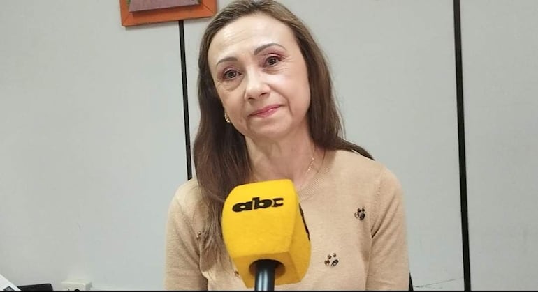 Mujer de cabello largo y castaño con micrófono amarillo, en un fondo interior claro, durante una entrevista.
