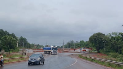 Camión circula por la carretera en construcción, con vegetación a ambos lados y clima nublado, sin personas visibles.