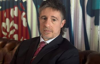 Rogelio Ortuzar sentado en un entorno moderno, vestido con traje oscuro y corbata de colores, con expresión reflexiva.