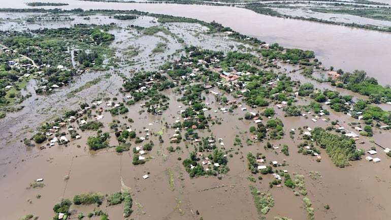 Vista aérea con casas parcialmente sumergidas en agua, rodeadas de vegetación y áreas anegadas, reflejando crisis ambiental.