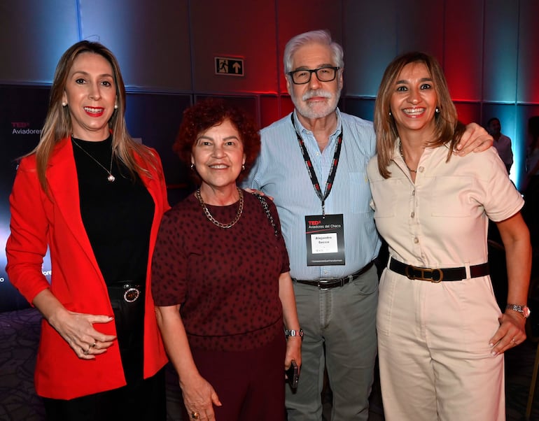 Alejandro Secco en el centro, rodeado de mujeres sonriendo, en un ambiente iluminado en rojos y azules, con logotipo TEDx al fondo.