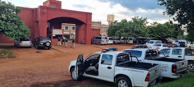 Policías uniformados conversan en la entrada de un edificio, mientras dos camionetas del Gobierno del Paraguay están estacionadas.