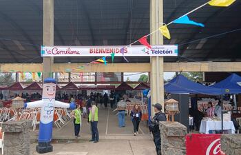 Asistentes en evento benéfico con chalecos de seguridad, mesas y banderines de colores, rodeados de stands de comida y un muñeco inflable.