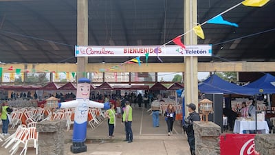 Asistentes en evento benéfico con chalecos de seguridad, mesas y banderines de colores, rodeados de stands de comida y un muñeco inflable.